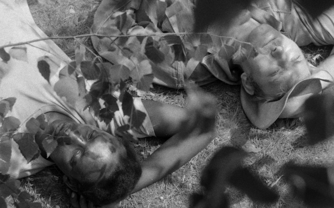 Filmstill aus JAGDPARTIE: Ein schwarzer und ein weißer Mann liegen nebeneinander im Gras.