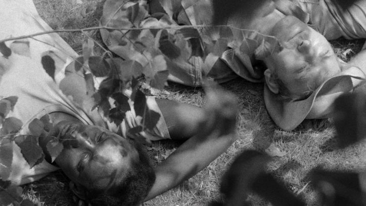 Film still from JAGDPARTIE: A black man and a white man are lying next to each other in the grass.