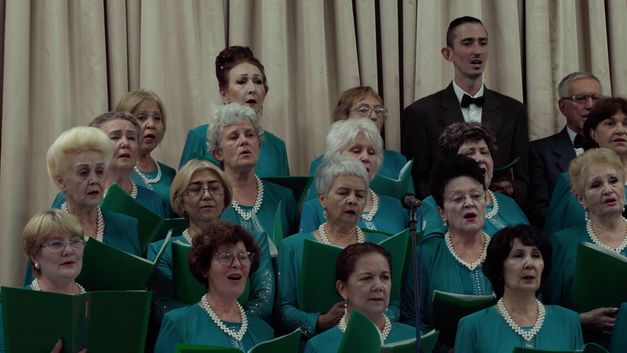 Film still from NAGOTA by Sabina Bakaeva. The picture shows singers of a choir dressed in uniform while singing. 