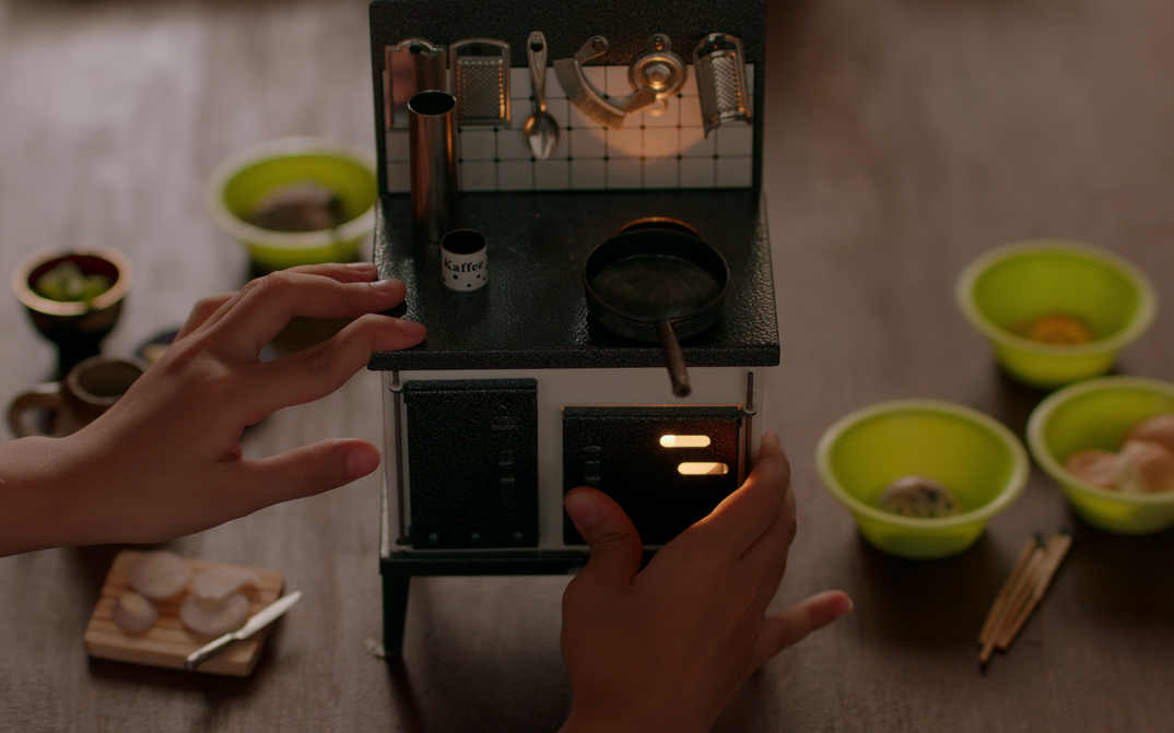 Filmstill aus NERVOUS TRANSLATION: Man sieht eine Puppenküche und zwei Kinderhände, die damit spielen.