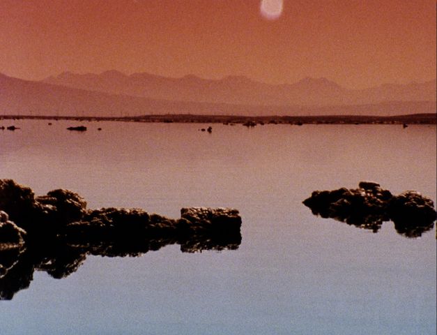 Still from the film "Instant Life" by Anja Dornieden, Juan David González Monroy and Andrew Kim. A body of water with rocks, mountains in the background
