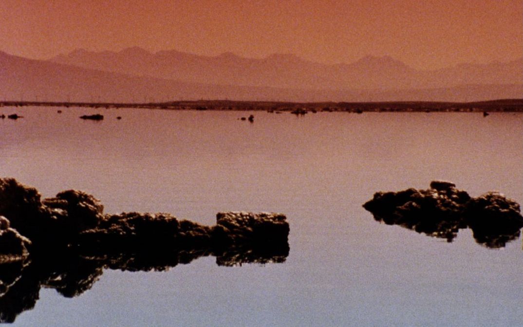 Still from the film "Instant Life" by Anja Dornieden, Juan David González Monroy and Andrew Kim. A body of water with rocks, mountains in the background