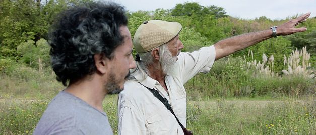 Still from the film "Camuflaje (Camouflage)" by Jonathan Perel. Two men in a shoulder close-up in profile. The older one points out something. 