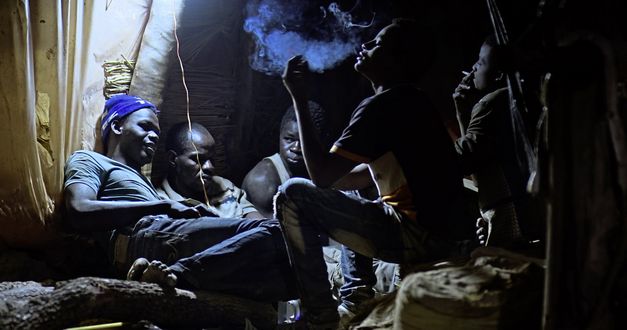 Filmstill aus „Or de vie“ von Boubacar Sangaré. Filmstill aus „Or de vie“ von Boubacar Sangaré. Fünf Männer sitzen in einem Goldsucher-Bergwerk. Die beiden Männer auf der rechten Seite rauchen eine Zigarette.