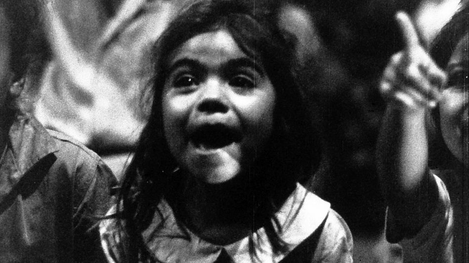 Filmstill aus POR PRIMERA VEZ: Ein kleines Mädchen mit begeistertem Gesichtsausdruck sitzt neben anderen Kinobesuchern.