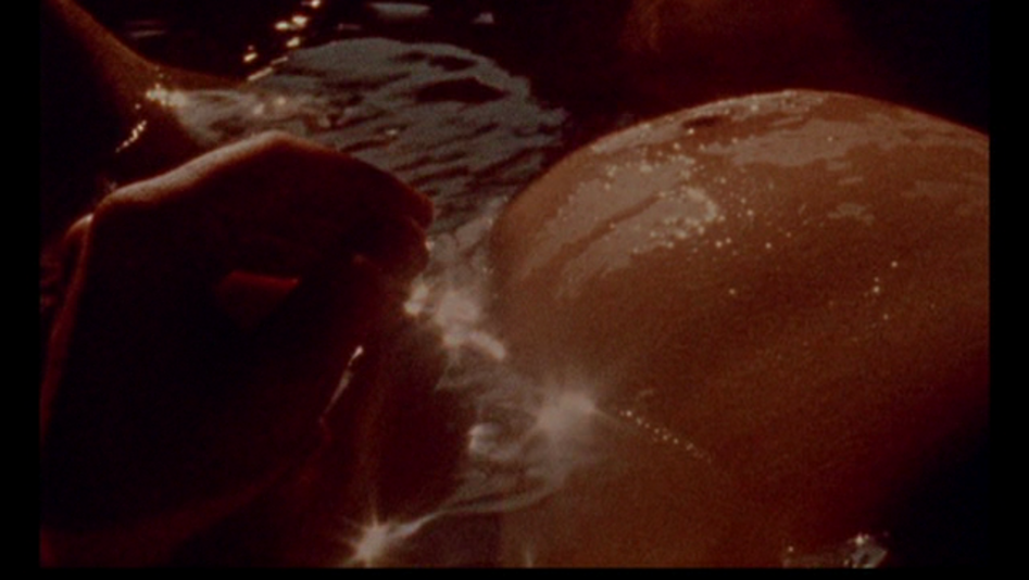 Filmstill aus WINDOW WATER BABY MOVING: Man sieht den Bauch einer Schwangeren im Wasser. Das Wasser glitzert durch einfallende Lichtstrahlen.