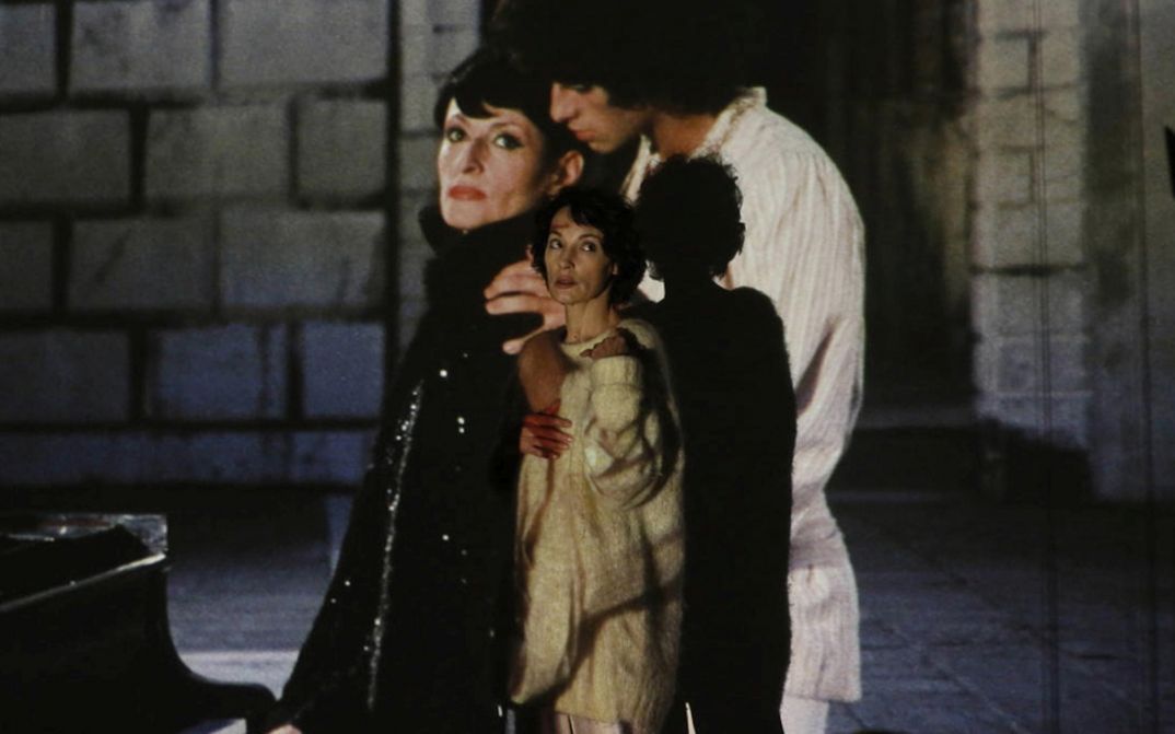 Film still from BARBARA. A woman stands in front of a screen on which a man and a woman are projected.