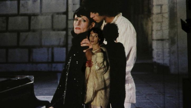 Filmstill aus BARBARA. Eine Frau steht vor einer Leinwand, auf die ein Mann und eine Frau projiziert sind.