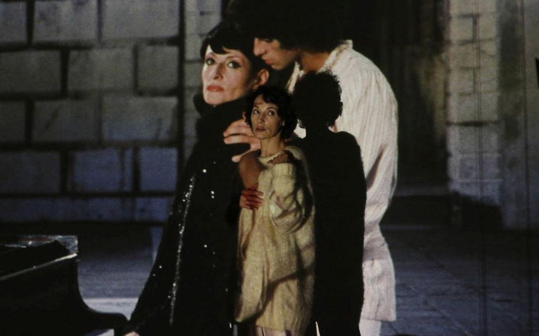 Filmstill aus BARBARA. Eine Frau steht vor einer Leinwand, auf die ein Mann und eine Frau projiziert sind.