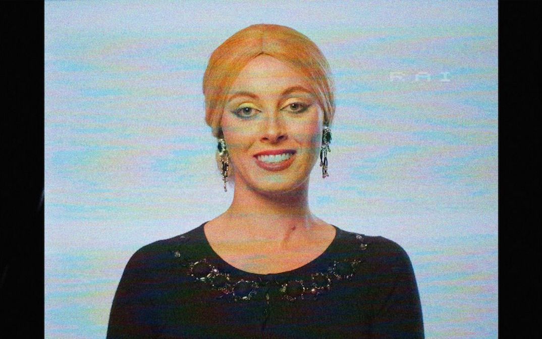 Film still from CORPO DI REATO: You see a flickering television picture of a woman smiling into the camera.