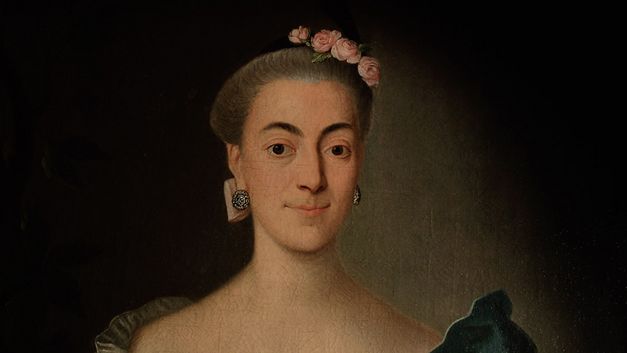 Filmstill aus "Ihre ergebenste Fräulein" von Eva C. Heldmann. Zu sehen ist eine Nahaufnahme des Bildes einer Frau mit hochgestecktem Haar, Blumen auf dem Kopf und runden Ohrringen. 