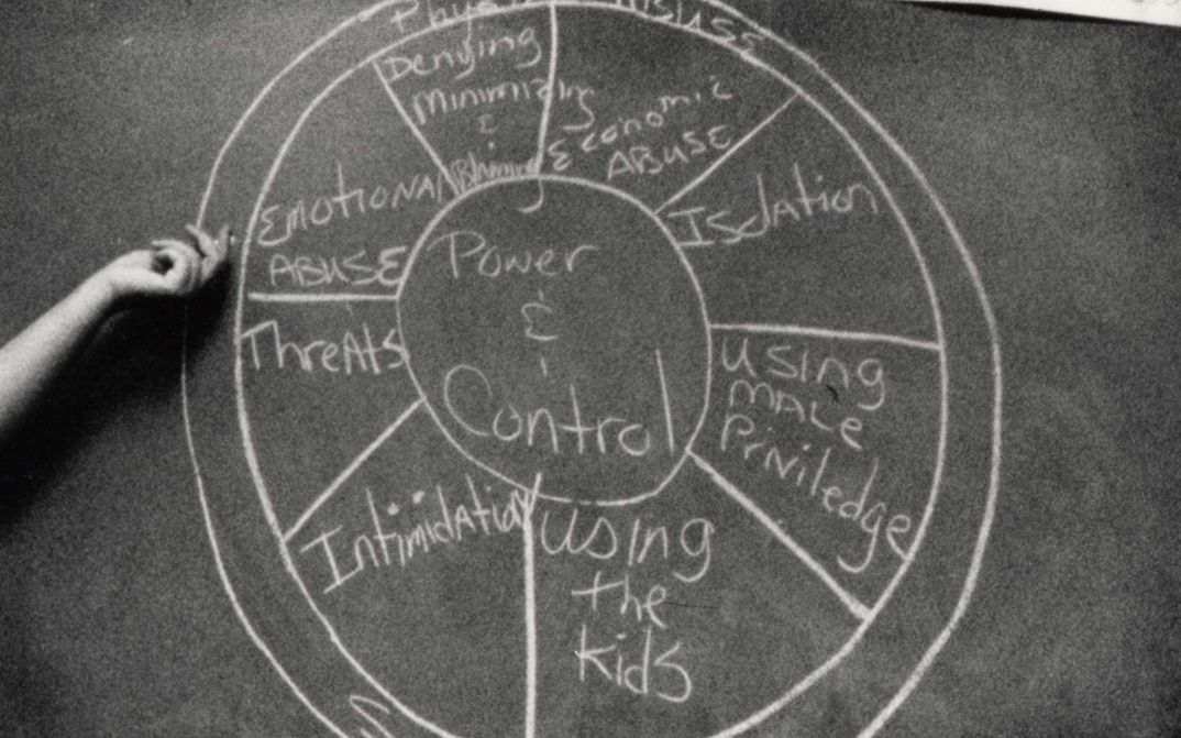 Film still from DOMESTIC VIOLENCE. On a blackboard, a diagram of domestic violence methods is drawn with chalk.
