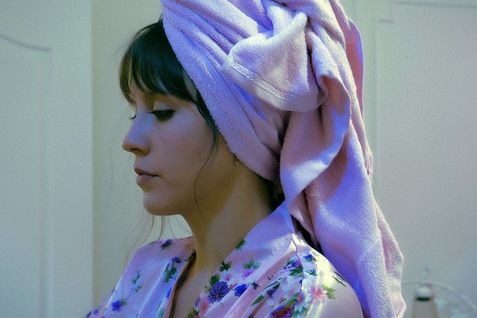 Filmstill aus ENDURANCE: Eine Frau mit dunklen Haaren im Profil. Sie trägt einen Bademantel und ein Handtuch um den Kopf.