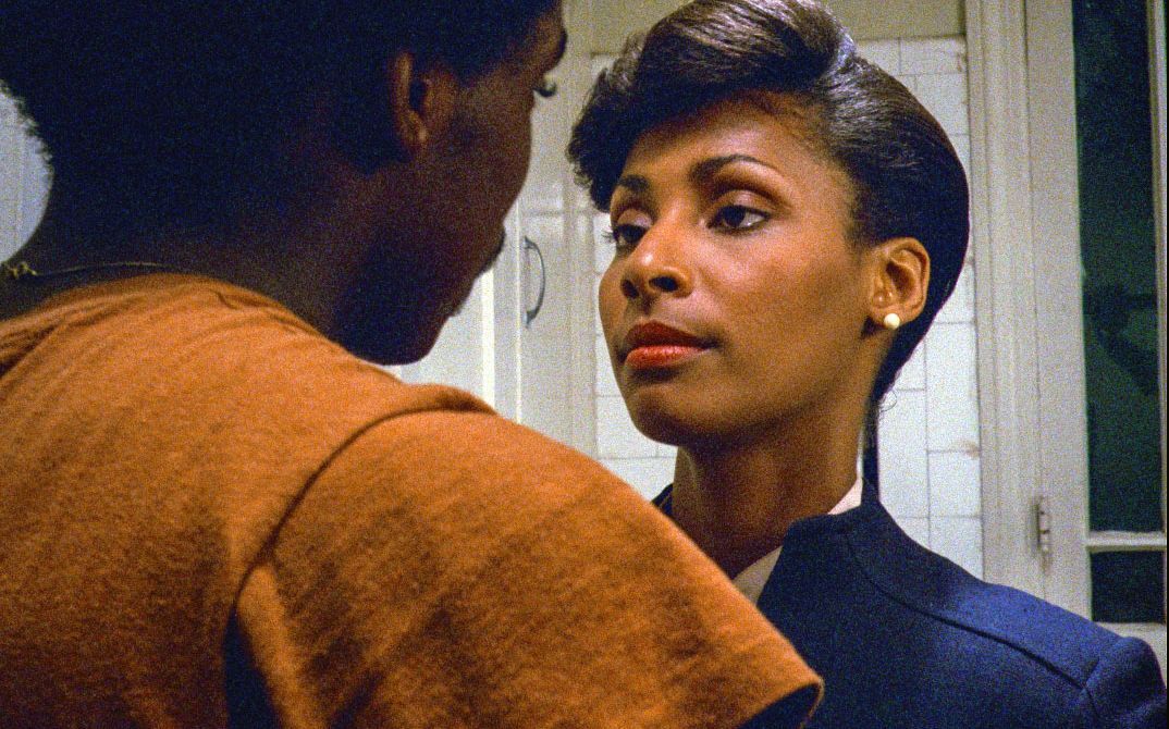 A woman and a man stand facing each other in a kitchen, looking at one another.