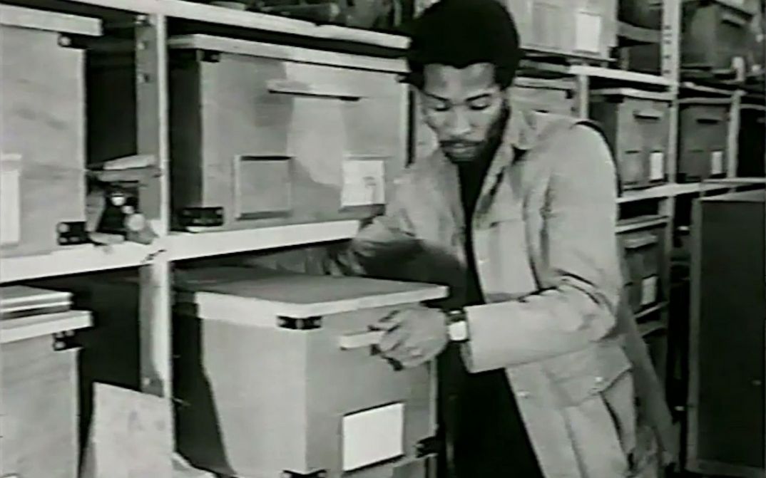 Filmstill aus YOU HIDE ME: Ein Mann zieht eine große Schachtel aus einem Regal.