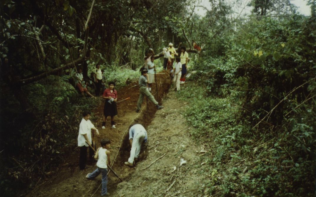 Filmstill aus BRIEFE AUS WIWILLI: Menschen graben eine Furche in einen Abhang. Um sie herum ist Wald.