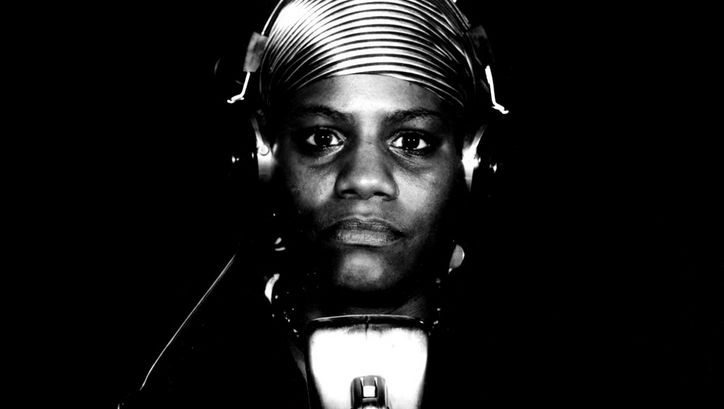 Film still from BORN IN FLAMES: A woman sits in front of a microphone with headphones in the radio studio.