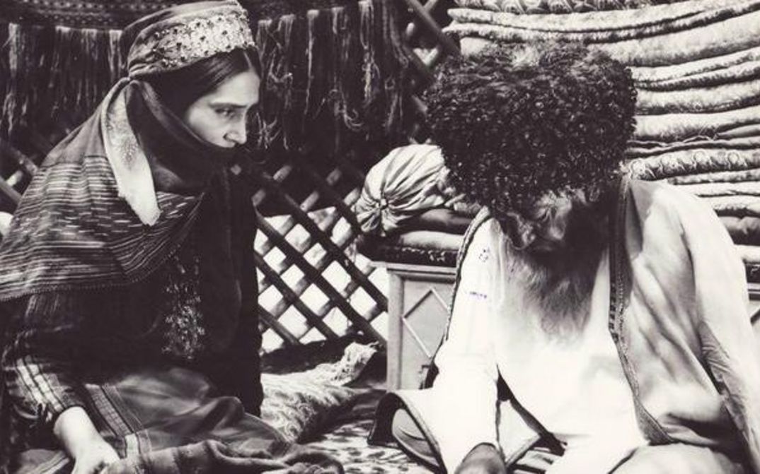 Film still from GELIN: A man and a woman, both in traditional Central Asian dress, are sitting on the floor.