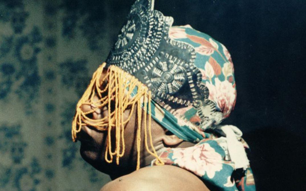 Film still from ÔRÍ: A person with a colourful cloth and headdress covering the face.