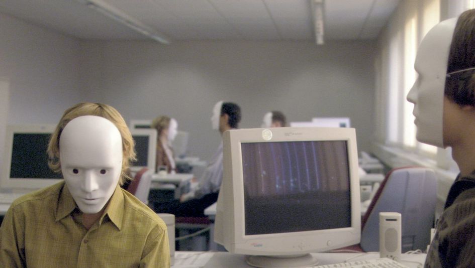 Film still from FALSCHER BEKENNER: Several people are sitting at computers in an open-plan office. They are all wearing white masks that cover their entire faces.