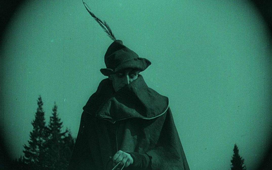Film still from NOSFERATU: Monochrome green colored picture of a man with coat and hat on a horse.