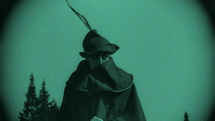 Filmstill aus NOSFERATU: Monochrom grün eingefärbtes Bild eines Mannes mit Mantel und Hut auf einem Pferd.