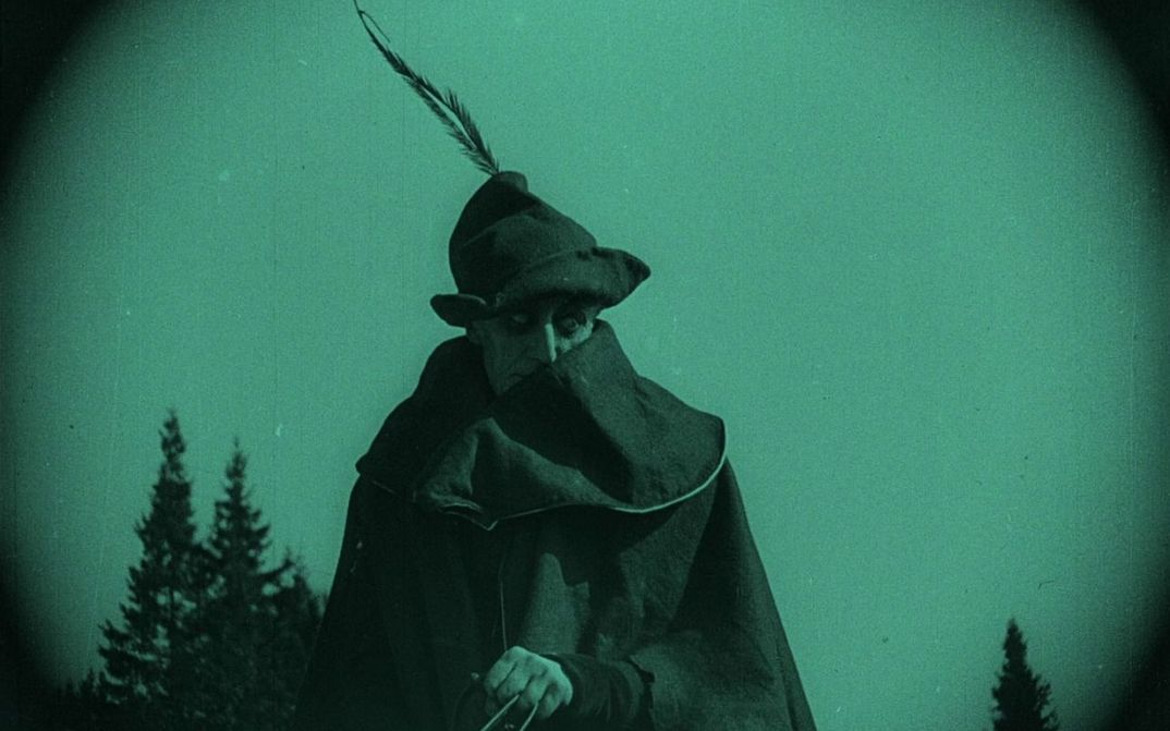 Filmstill aus NOSFERATU: Monochrom grün eingefärbtes Bild eines Mannes mit Mantel und Hut auf einem Pferd.