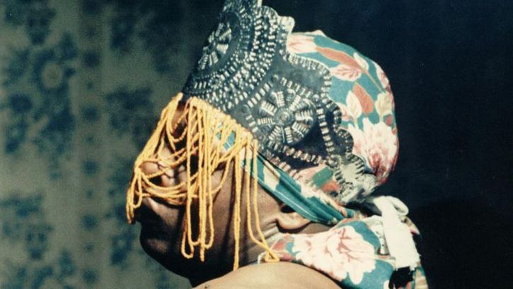 Film still from ÔRÍ: A person with a colourful cloth and headdress covering the face.