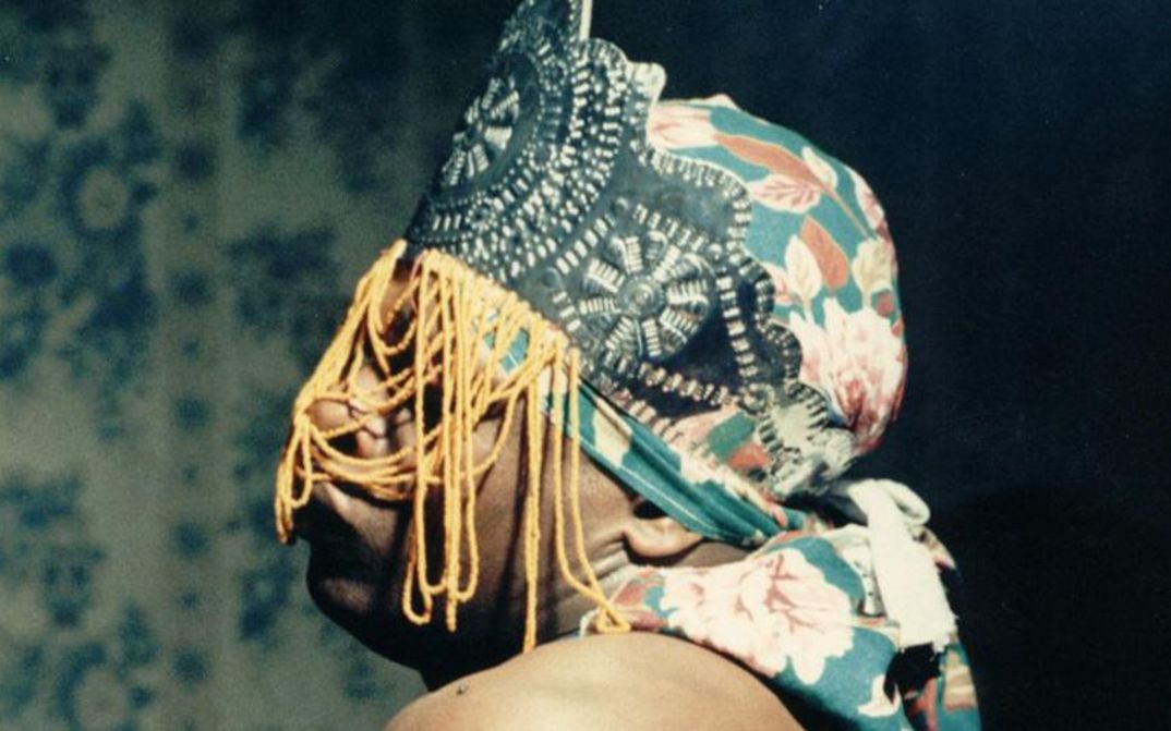 Film still from ÔRÍ: A person with a colourful cloth and headdress covering the face.