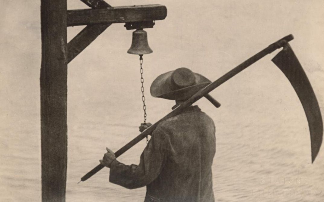 Filmstill aus VAMPYR: Man sieht von hinten einen Mann mit Hut und einer Sense, der an Glocke klingelt.