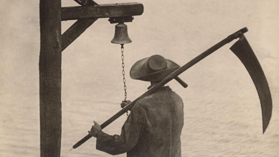 Film still from VAMPYR: From behind, you can see a man wearing a hat and holding a scythe, ringing a bell.