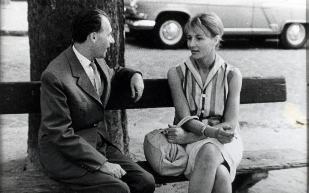 A man and a woman sit on a park bench talking to each other.