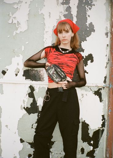 Teenager with red scarf on head in street style clothes stands in front of a wall