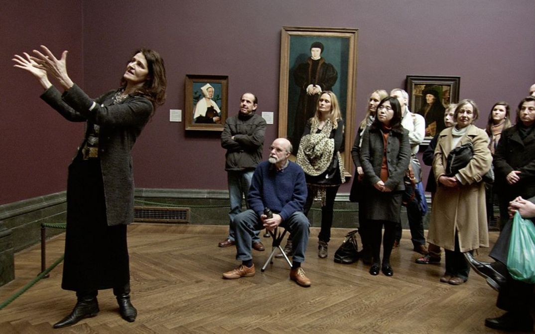 Filmstill aus NATIONAL GALLERY. Eine Frau erklärt einer Gruppe von Museumsbesuchern ein Kunstwerk.