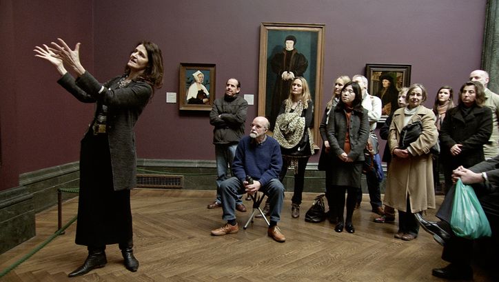 Film still from NATIONAL GALLERY. A woman explains a work of art to a group of museum visitors.