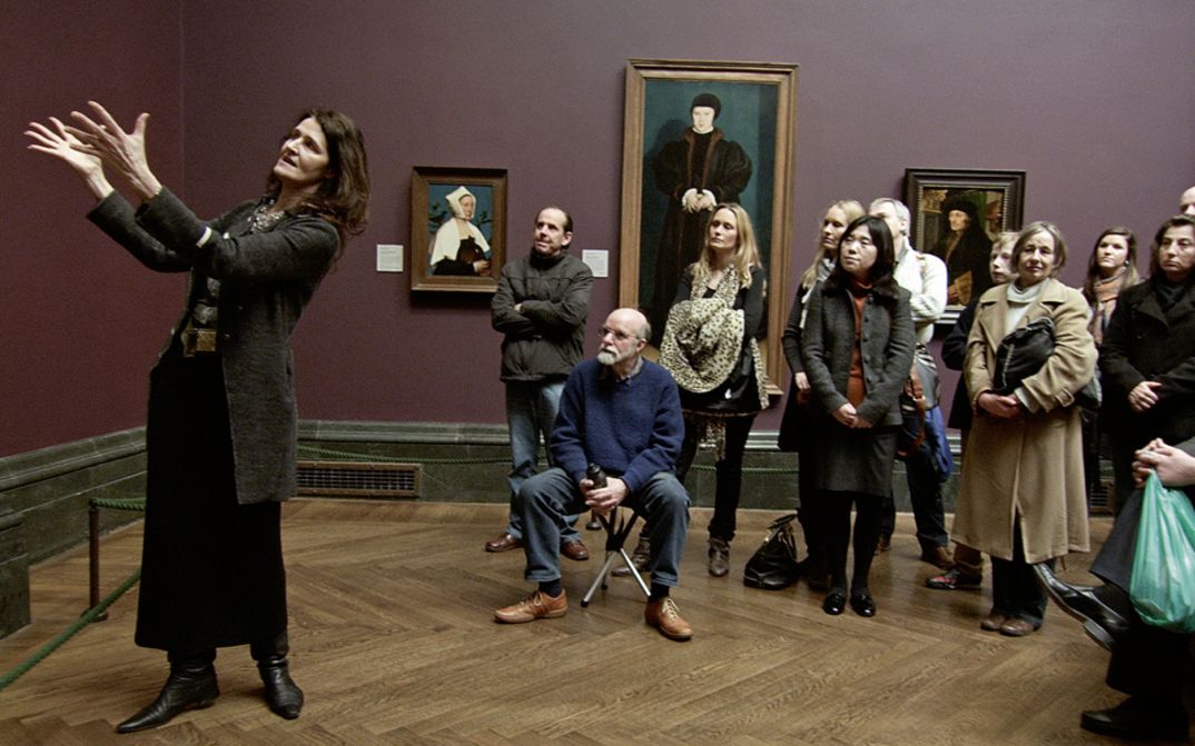 Filmstill aus NATIONAL GALLERY. Eine Frau erklärt einer Gruppe von Museumsbesuchern ein Kunstwerk.