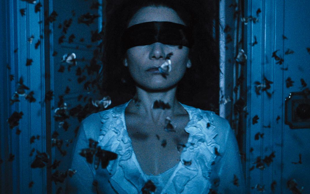 Filmstill aus THE DUKE OF BURGUNDY: Eine Frau mit verbundenen Augen, umschwirrt von Schmetterlingen.