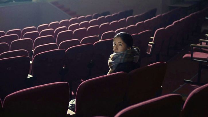 Still from the film "Akyn (Poet)" by Darezhan Omirbayev. A woman sitting alone in an empty theatre is turned and facing the back of the room.