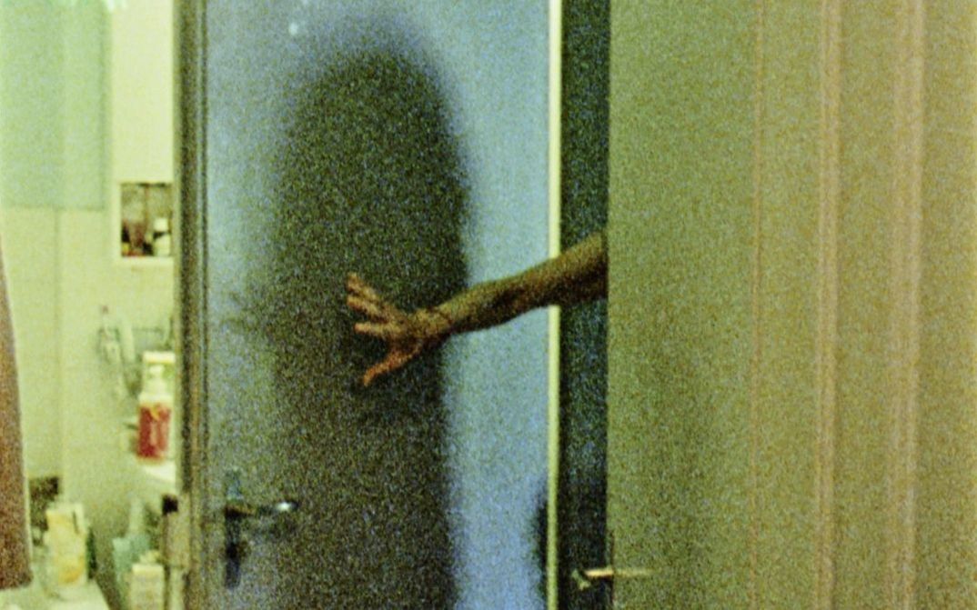 Filmstill aus "Spuren von Bewegung vor dem Eis" von René Frölke. Zu sehen ist ein Badezimmer. Die Badezimmertür wird von einem Arm offen gehalten.