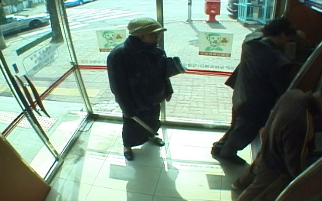 Film still from INFLUENZA: You see the recording from a surveillance camera, people at ATMs.