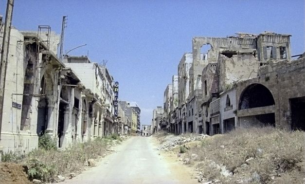 Filmstill aus „Beirut al lika (Beirut the Encounter)“ von Borhane Alaouié. Eine leere Straße gesäumt von Häusern in Ruinen. 