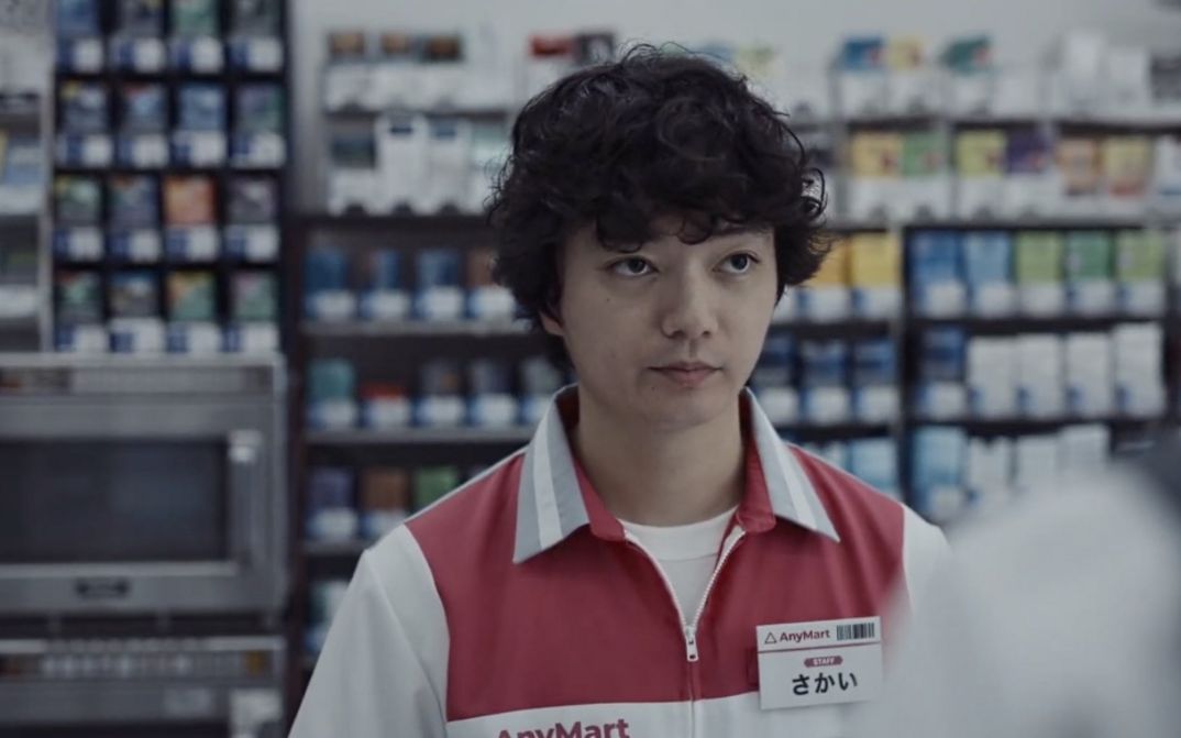 Young person in supermarket uniform looks straight toward unseen customer.