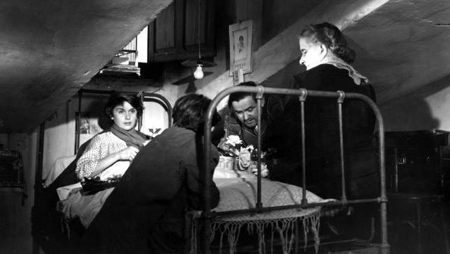 Filmstill aus SEGUNDO LOPEZ, AVENTURERO URBANO: In einer Dachkammer liegt eine kranke junge Frau im Bett. Drei Menschen stehen um das Bett herum.