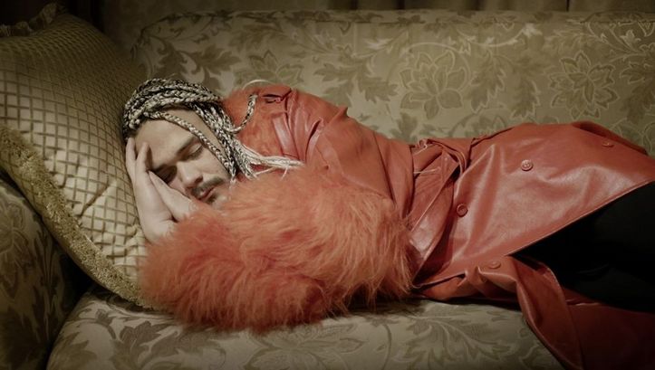 Still from the film „Llamadas desde Moscú“ by Luís Alejandro Yero. A man in a red coat is sleeping on a sofa.