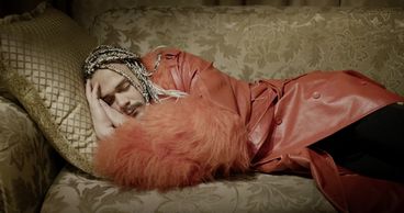 Still from the film „Llamadas desde Moscú“ by Luís Alejandro Yero. A man in a red coat is sleeping on a sofa.