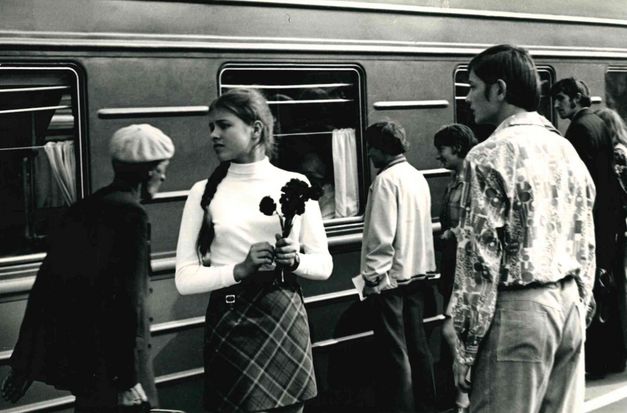 Filmstill aus DER SPECHT ZERBRICHT SICH NICHT DEN KOPF: Einige Menschen stehen an einem Bahnsteig, hinter sich ein stehender Zug. Ein junges Mädchen hält Blumen in der Hand und blickt sehnsuchtsvoll in die Ferne.