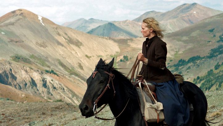 Filmstill aus GOLD: Eine Frau sitzt auf einem Pferd und blickt in die Ferne. Im Hintergrund sind Berge.