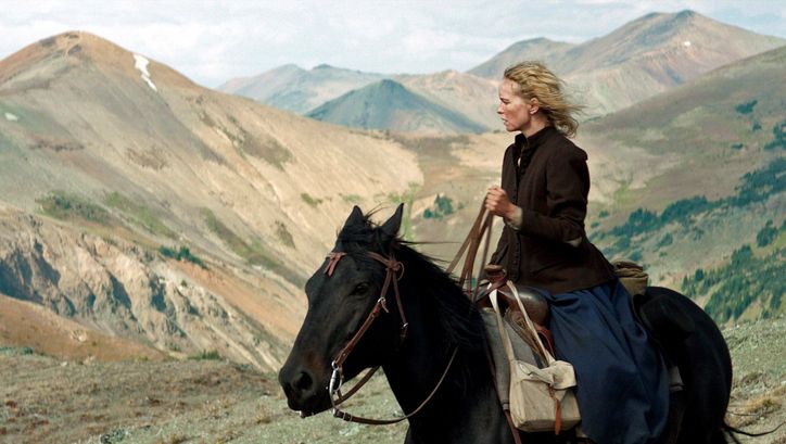 Filmstill from GOLD: A woman sits on a horse and looks into the distance. There are mountains in the background.