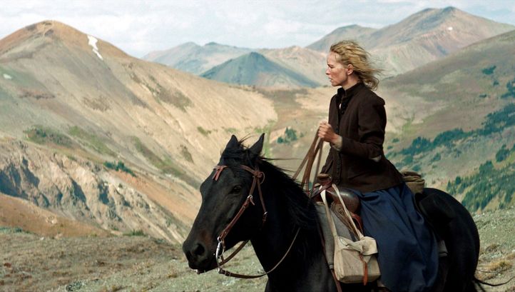 Filmstill aus GOLD: Eine Frau sitzt auf einem Pferd und blickt in die Ferne. Im Hintergrund sind Berge.