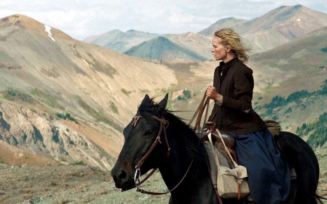Filmstill aus GOLD: Eine Frau sitzt auf einem Pferd und blickt in die Ferne. Im Hintergrund sind Berge.